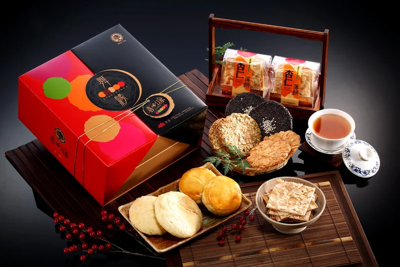 紅黑食品禮盒搭配杏仁薄餅、芝麻餅及糕餅，與茶杯和木質道具組合陳列