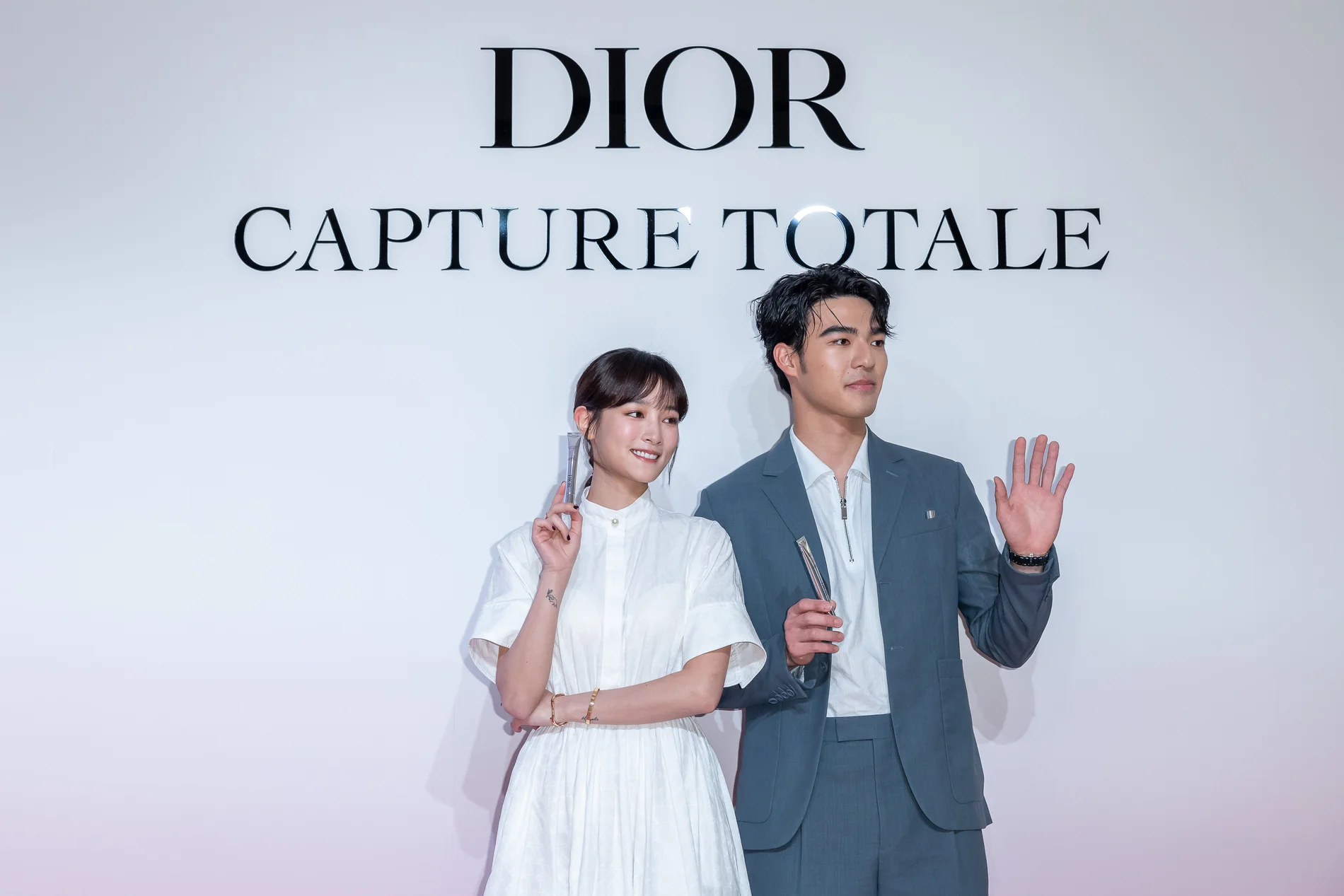 王淨與陳昊森手持產品,在 DIOR 與 CAPTURE TOTALE 品牌背板前合影