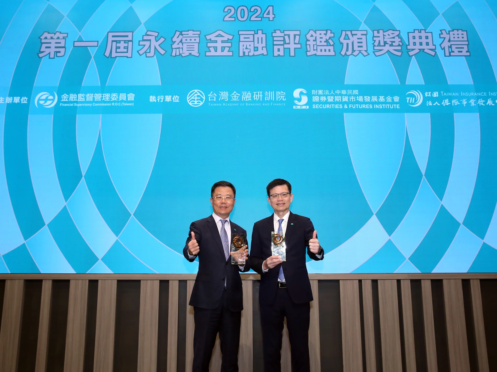 國泰世華銀行兩位代表手持獎座在第一屆永續金融評鑑舞台合影