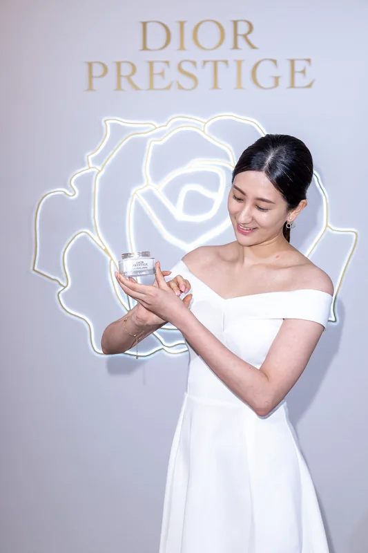 DIOR品牌代言人賈靜雯穿白色禮服，微笑注視手中的精萃再生保養品