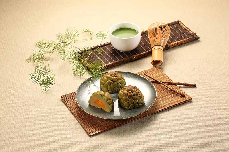 金釋迦造型糕點置於圓盤，搭配抹茶茶碗及竹筅的俯視情境